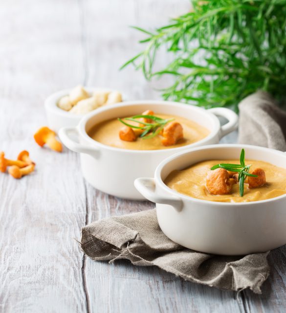 Mushroom cream soup with chanterelles and herbs on a white rustic wooden background, selective focus
