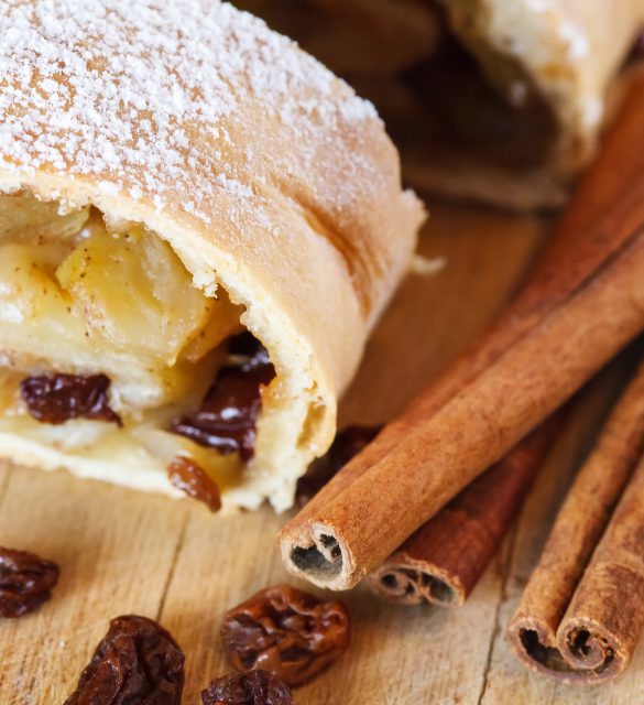 Apple strudel with icing sugar, cinnamon sticks, wooden background Apple strudel with icing sugar, cinnamon sticks, raisins, wooden background