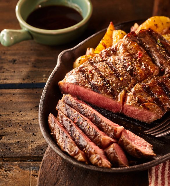 Cast iron plate with sliced grilled rib-eye steak on table Cast iron plate with sliced grilled rib-eye steak on table with yellow potato wedges and oil in saucer over table with copy space