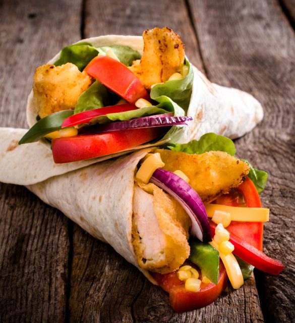 Tortilla wrap sandwich with fried chicken and vegetables on wooden background,selective focus