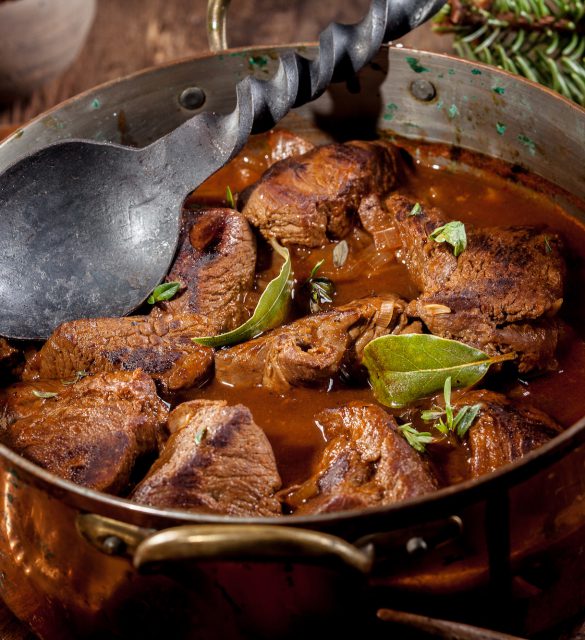 Venison Goulash Stew in Pot with Serving Spoon Large Metal Serving Spoon in Copper Pot of Venison Goulash Stew with Fresh Herbs Surrounded by Evergreen Sprigs and Deer Antlers