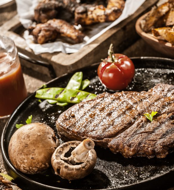 Rustic country meal of grilled rib eye beef steak Rustic country meal of grilled ribe eye beef steak with mushrooms and tomato served with homemade ketchup and assorted barbecued meats on a summer picnic