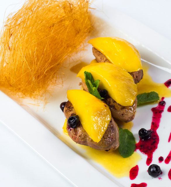 Pan seared foie gras on ripe mango and pomegranate reduction. white plate Pan seared foie gras on ripe mango and pomegranate reduction on white plate.