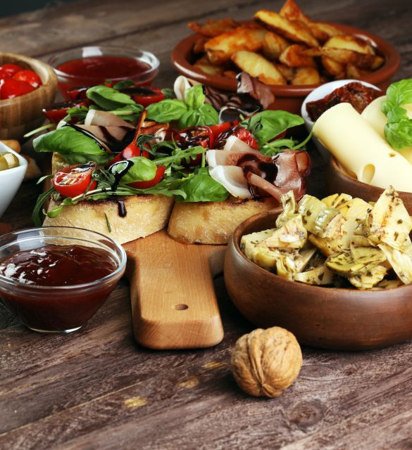 Italian antipasti wine snacks set. Cheese variety, Mediterranean olives, pickles, Prosciutto di Parma, tomatoes, artichokes and wine in glasses over black grunge background