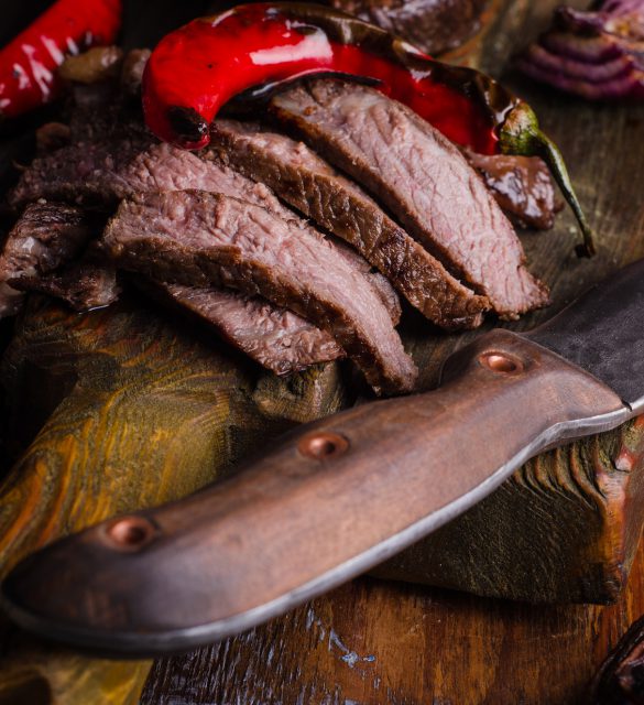 Sliced medium rare grilled Beef steak with chili pepper and ketchup on cutting board on wooden background. Slice of steak. Selective focus Medium rare grilled Beef steak Ribeye with knife and fork for meat on cutting board on dark wooden background