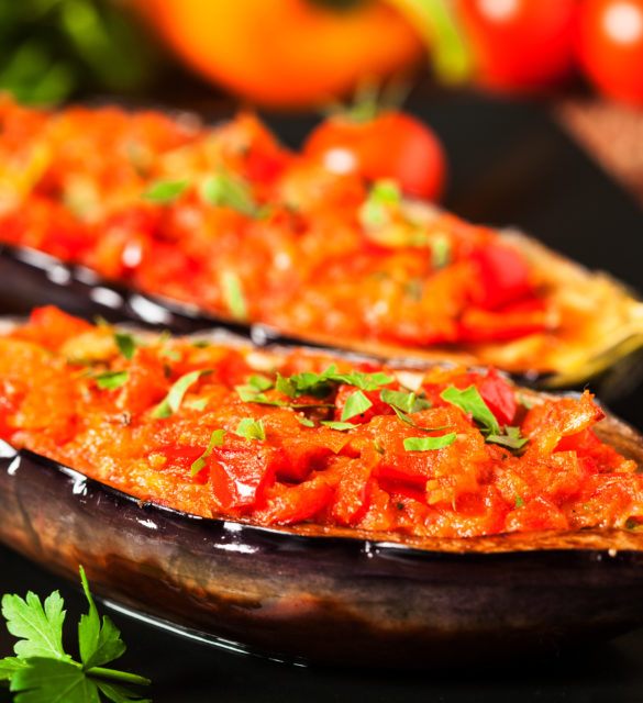 Stuffed aubergine on black plate. Wooden background. Front view.